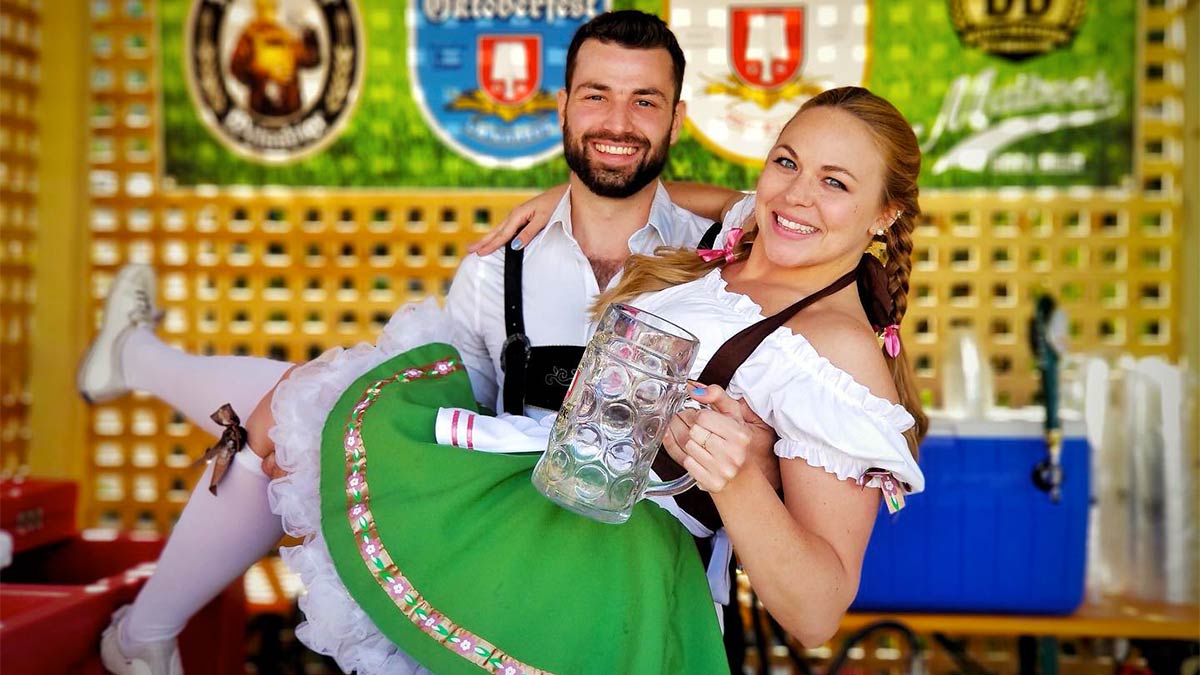 friends in festive attire posing for photo with woman holding beer mug and colorful posters in background at Wunder Gartens 7th Annual Oktoberfest Celebration in Washington DC, USA