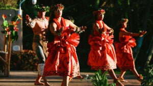 Three women and one men performing on stage with Hawaiian outfit.