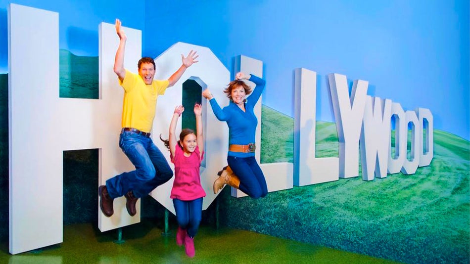 A parent with their daughter doing a jump post with a "Hollywood" background