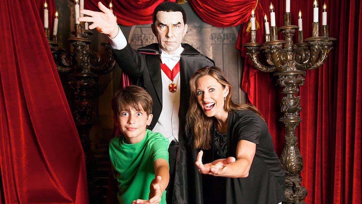 A male kid and an adult woman have a photo with a vampire statue.