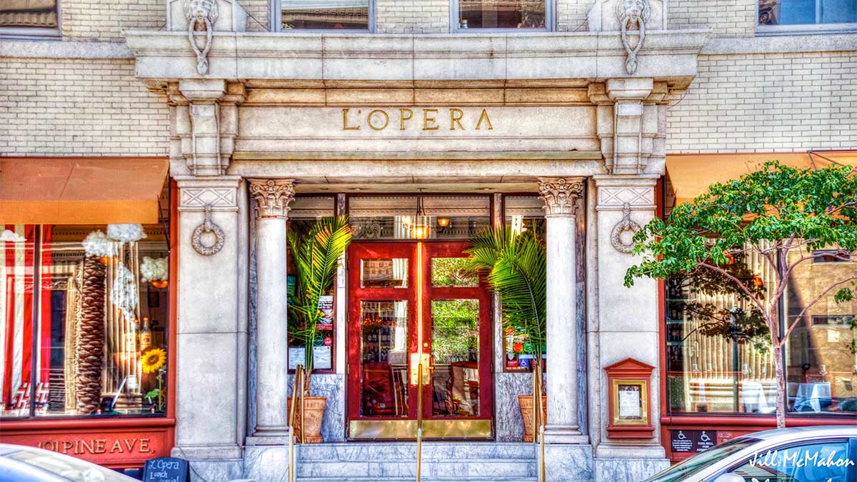 close up of entrance to LOpera Italian Restaurant with red doors during day and cars on street on foreground in Long Beach, California, USA