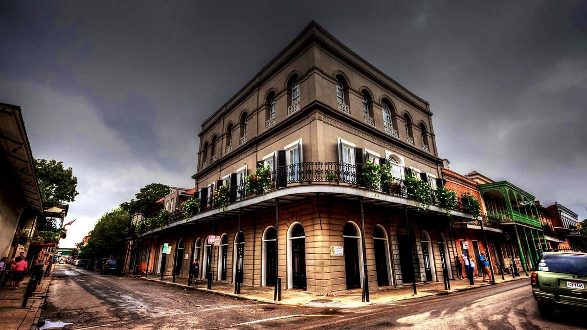 angled shot of exterior of LaLaurie Mansion with view of street and surrounding establishments on cloudy day in New Orleans, Louisiana, USA