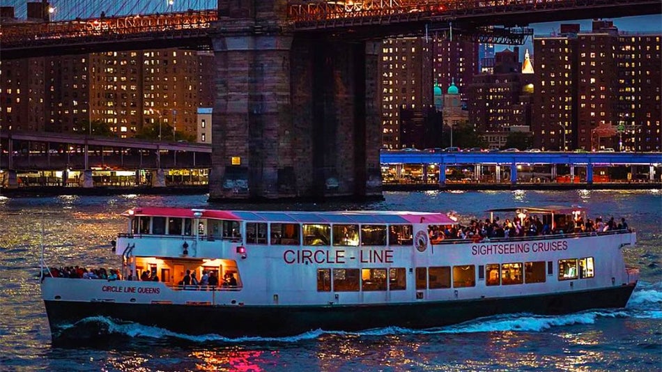 boat on water with people aboard and bridge and buildings in background at night at NYC Harbor Lights Night Cruise in New York City, New York, USA