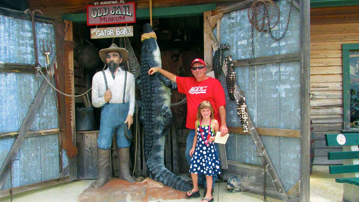  A photo of two people, a father and a daughter, beside a statue of a man and a dead crocodile.