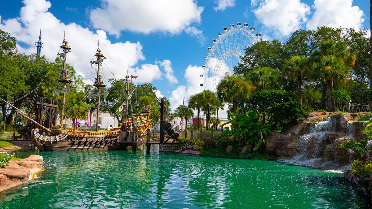 wideshot of pool and ship and waterfall on side with ferris wheel in background on a sunny day with blue sky and clouds at Pirates Cove Adventure Golf Orlando in Orlando, Florida, USA