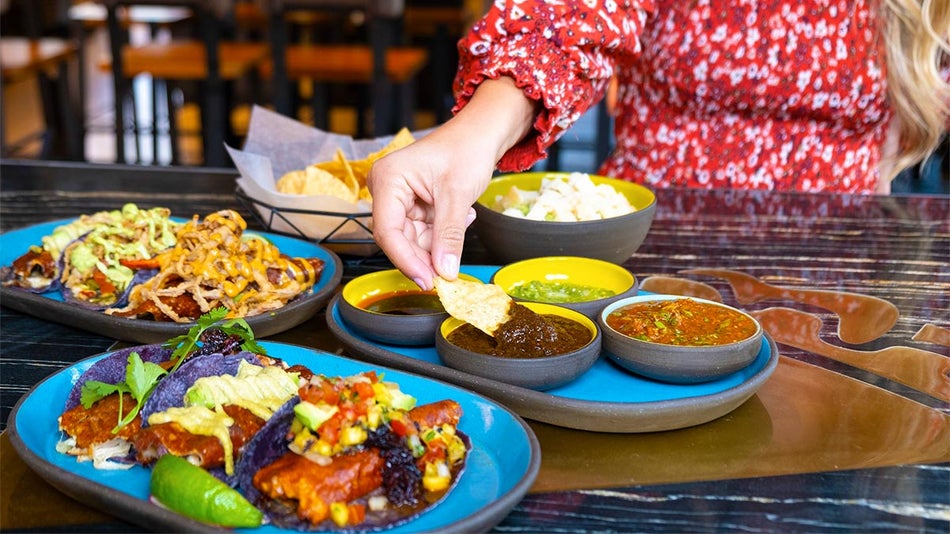 A woman eats three different types of Mexican food with three different sauces. 
