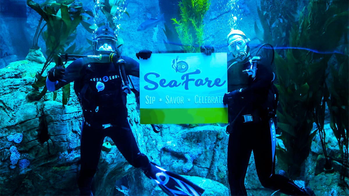 two divers in aquarium holding sign at SeaFare Aquarium of the Pacific in Los Angeles, California, USA
