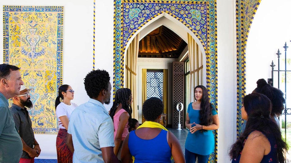 people gathered around a tour guide inside a museum with brightly painted trim around an entryway 