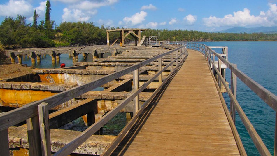 wooden pier with view of water and trees in distance on sunny day with blue sky and clouds at Ahukini Recreation Pier State Park in Kauai, Hawaii, USA