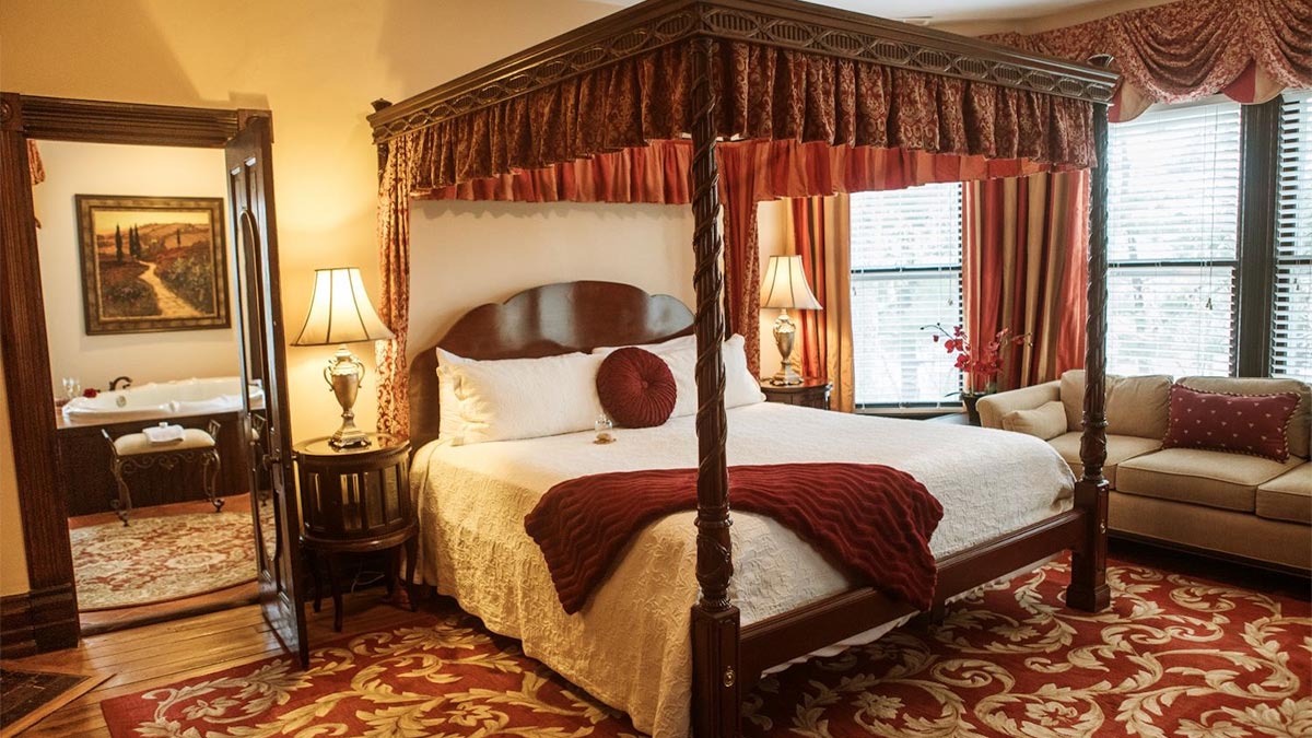 guest room with four poster bed, rug, couch, side table with lamp, and door opening to bathroom with bathtub at Biltmore Estate Vanderbilt Room (The Inn) in Asheville, North Carolina, USA