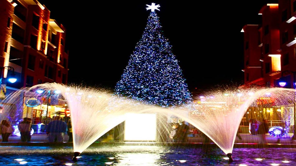 water fountain with christmas trees in background in the middle of two buildings at night at Branson Landing Winter Wonderland in Branson, Missouri, USA