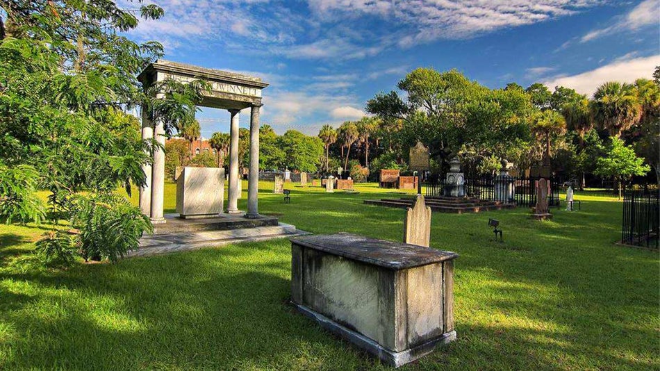 Daytime view of stone graves on a green lawn with trees surrounding under a blue sky with clouds