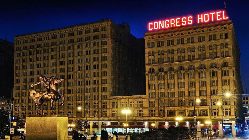 exterior of Congress Plaza Hotel at night with neon red sign and street lamps on ground and statue of man on horse in foreground in Chicago, Illinois, USA