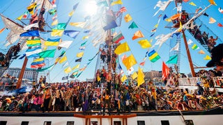 people in costume on boat with colorful banners and flags at Gasparilla Pirate Fest during sunny day in Tampa, Florida, USA