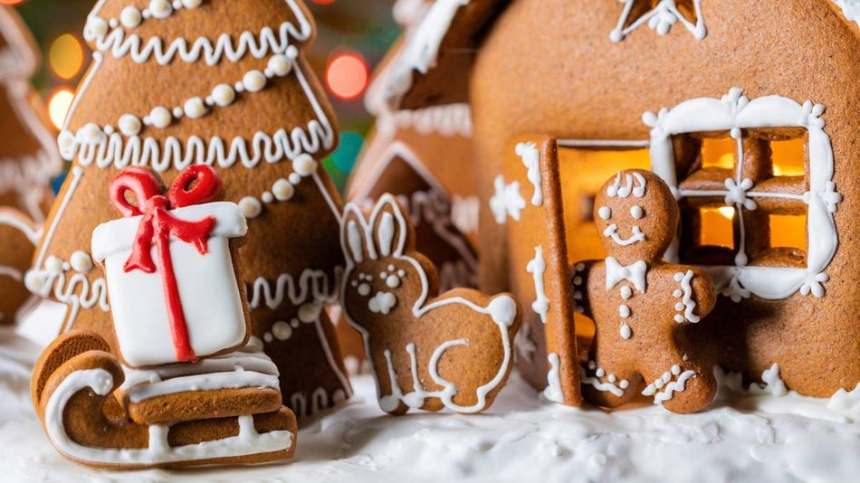 gingerbread man coming out of the door of his gingerbread house with a gingerbread bunny, sleigh, and tree all on white icing.