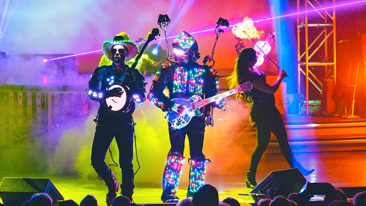 three performers on stage with lights attached to their suits as they play instruments