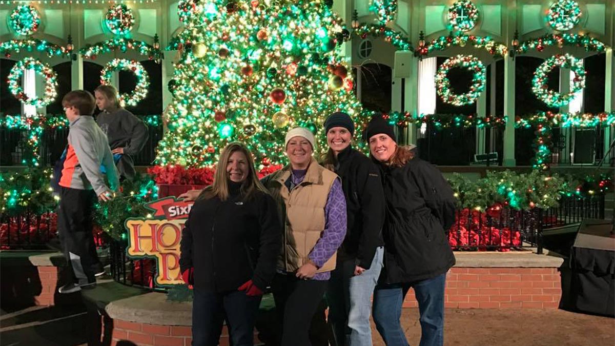people posing for photo with lit up chirstmas tree and christmas decorations background at Holiday in the Park Six Flags in Atlanta, Georgia, USA