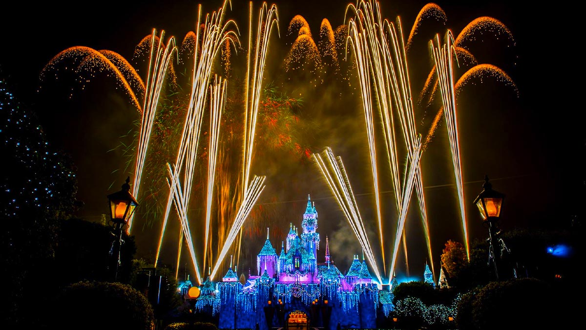 disney castle lit up with colorful lights with fireworks in sky at night during new years eve at Disneyland Resort in Los Angeles, California, USA