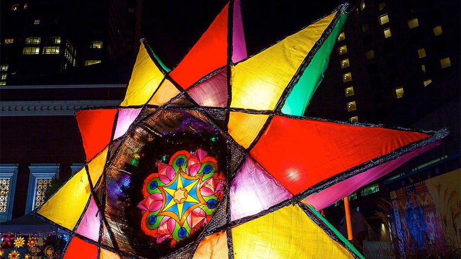close up of lit up multi-colored parol with buildings in background at night for Parol Lantern Festival and Parade in San Francisco, California, USA
