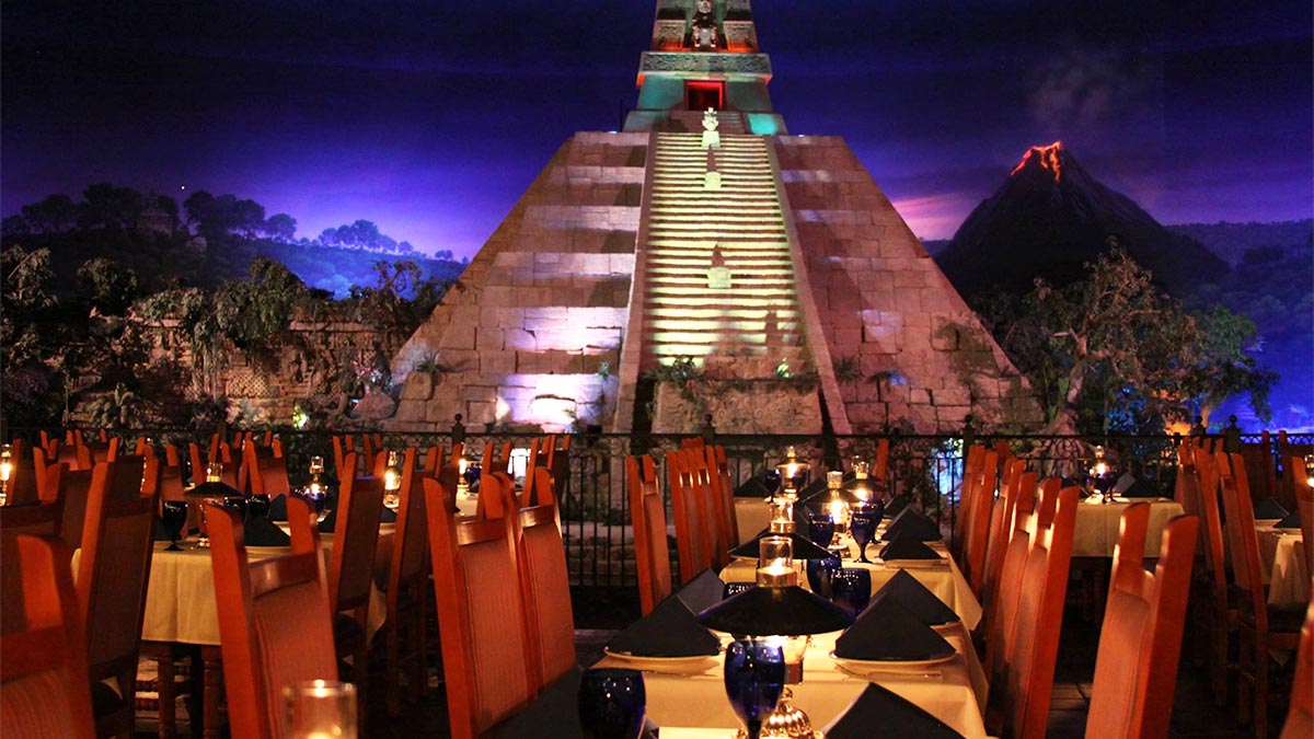 outdoor dining area with set tables and chairs with view of temple and volcano at night at Epcot in Orlando, Florida, USA