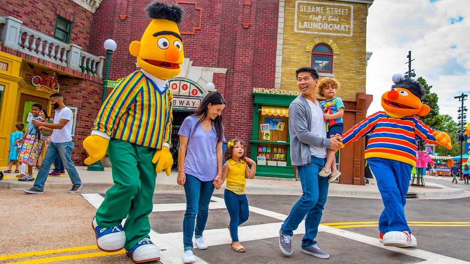 family crossing street with sesame street character mascots with buildings and people in background at Sesame Street Kids Weekends Seaworld Orlando in Orlando, Florida, USA