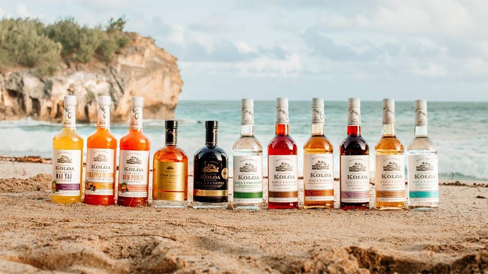 A line of different flavors of Koloa Rum Company bottles on the beach with the water behind them on a sunny day in Kauai, Hawaii, USA.