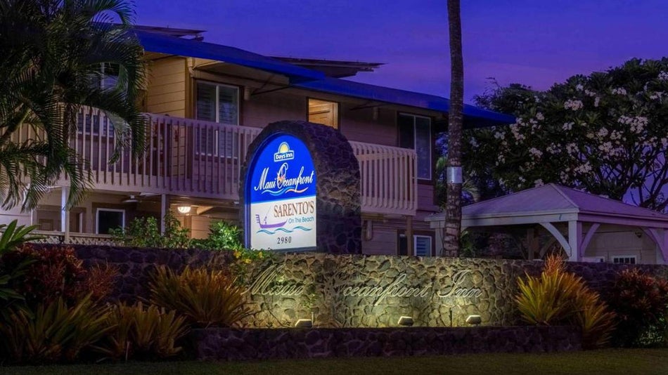 The sign for Days Inn by Wyndham Maui Oceanfront on a stone wall at night with the hotel in the background in Maui, Hawaii, USA.
