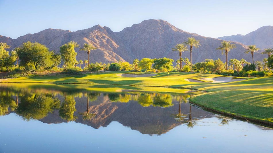 green golf course with reflective pond and palm trees with desert mountains in the background