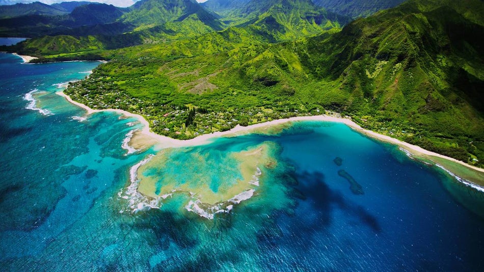 erial photo of reef and ocean at Tunnels beach with green mountains in the background