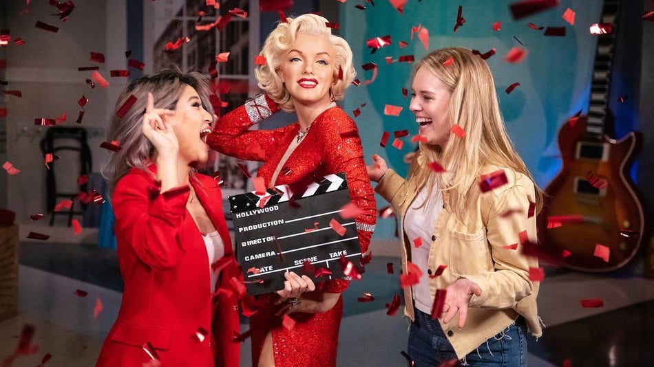 Marilyn monroe in a red dress holding a clapperboard surrounded by two girls at madame tussauds san francisco