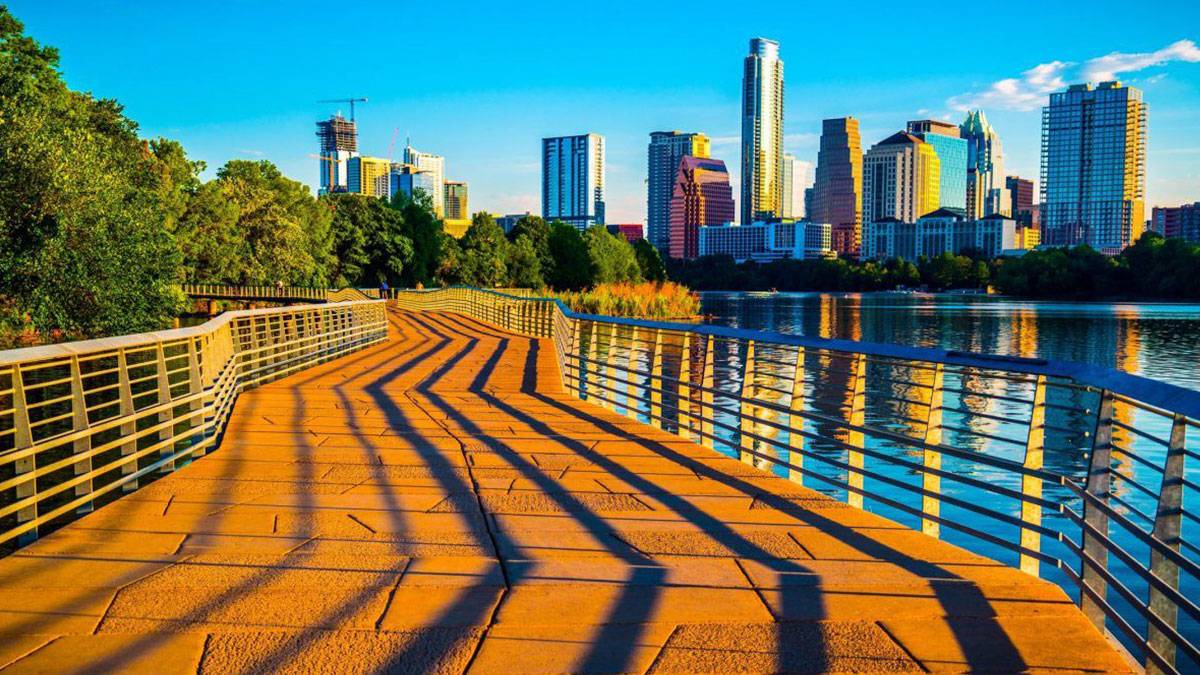 Golden brown walkway near lake with Austin, Texas skyline in background on a sunny day