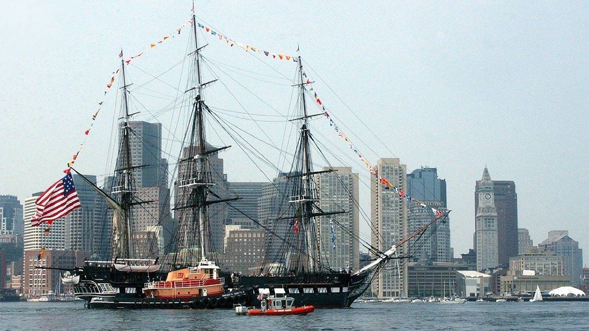USS Constitution floating in the Boston Harbor with buildings in the background