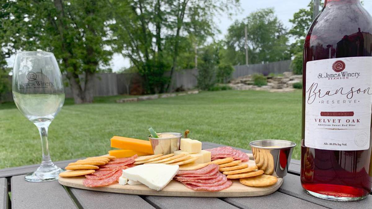 Close up of a meat and cheese board with a bottle of wine to the right and a glass to the left with a lawn in the back ground at Branson St James Winery & Restaurant in Branson, Missouri, USA