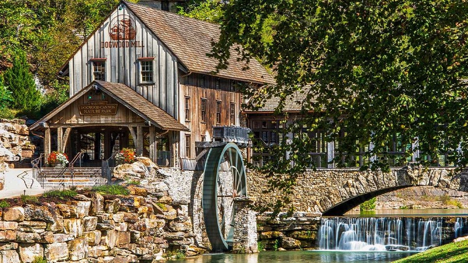 Front of the Dogwood Canyon Mill with the aged wooden exterior and water running next to it and a stone bridge in Branson, Missouri, USA