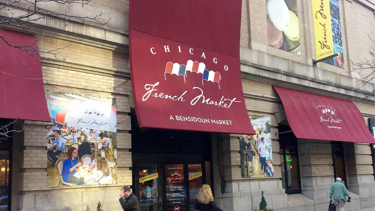Close up of the maroon cloth sign for the Chicago French Market hanging over the entrance with people walking under it in Chicago, Illinois, USA
