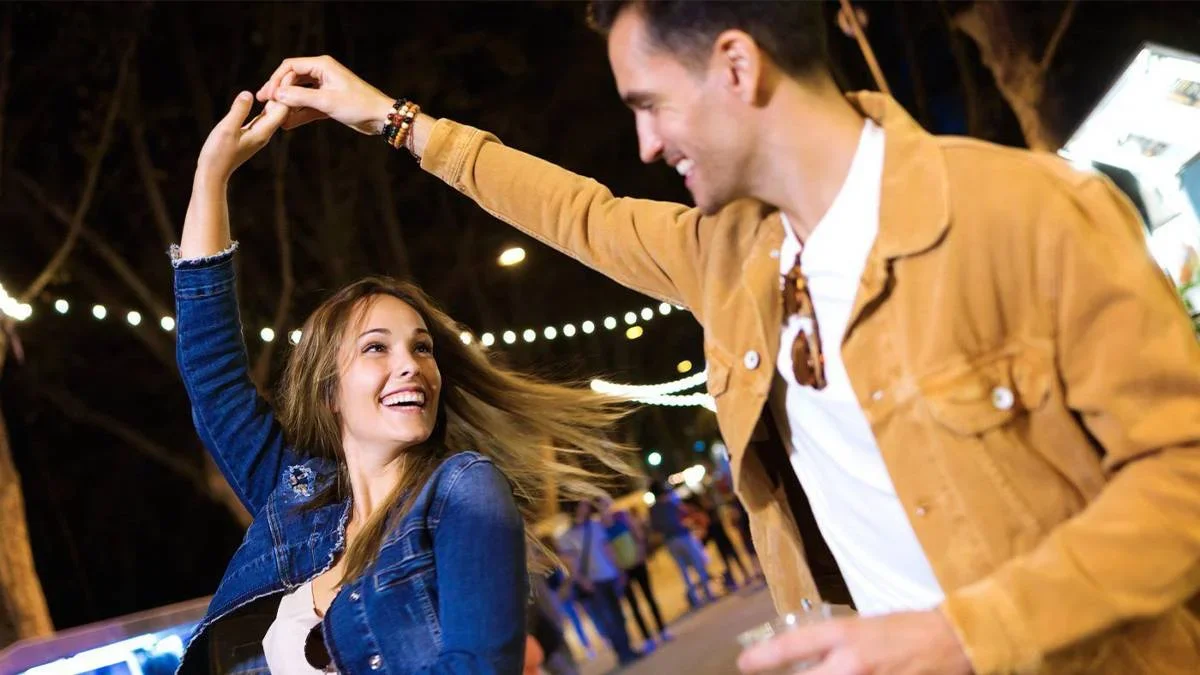 Carefree young couple dancing holding hands in eat market in the street at night.