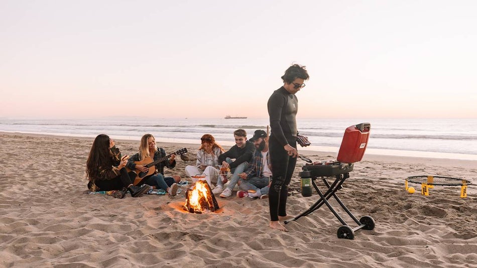 A group of friends having a bonfire and barbecue on the beach at sunset with the ocean in the background