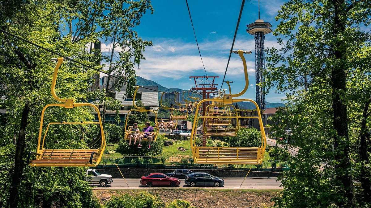 People riding the Gatlinburg Sky Lift with cars driving under them on a sunny day - Gatlinburg, Tennessee, USA