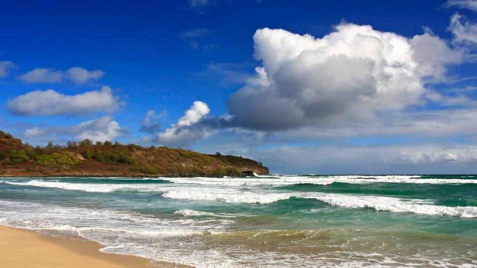 green waves with mild surf coming up onto the sand at kahili beach kauai