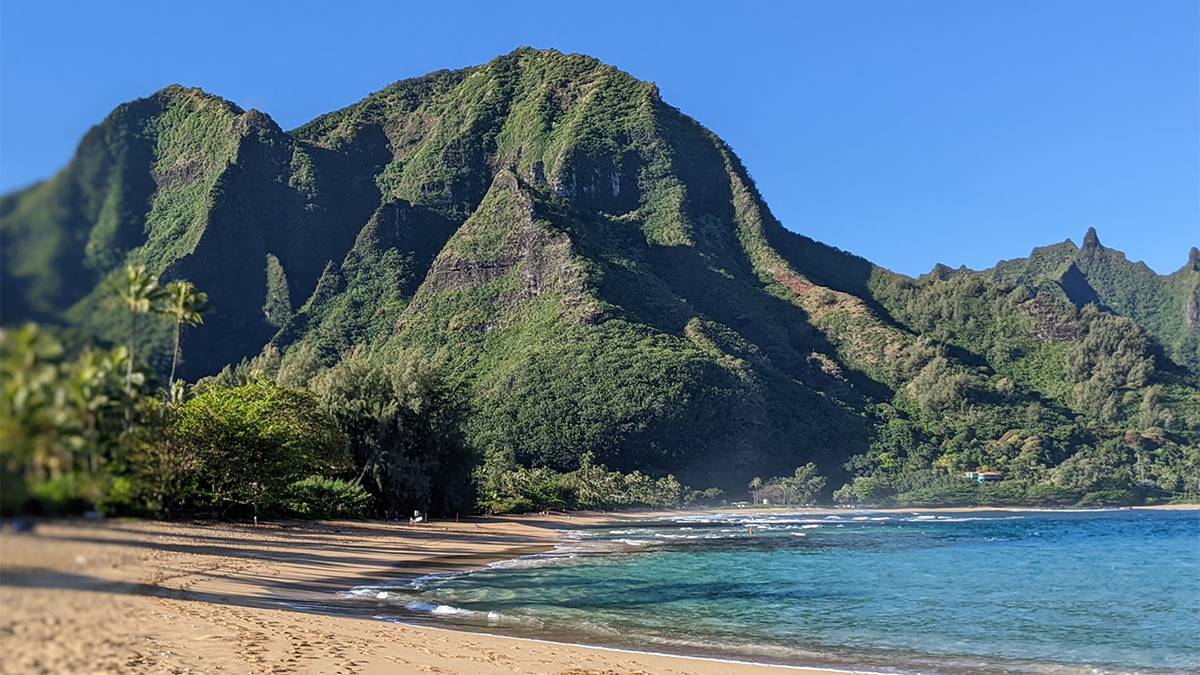 Ground view of sandy beach and ocean waves with trees in background at Tunnels Beach in Kauai, Hawaii, USA