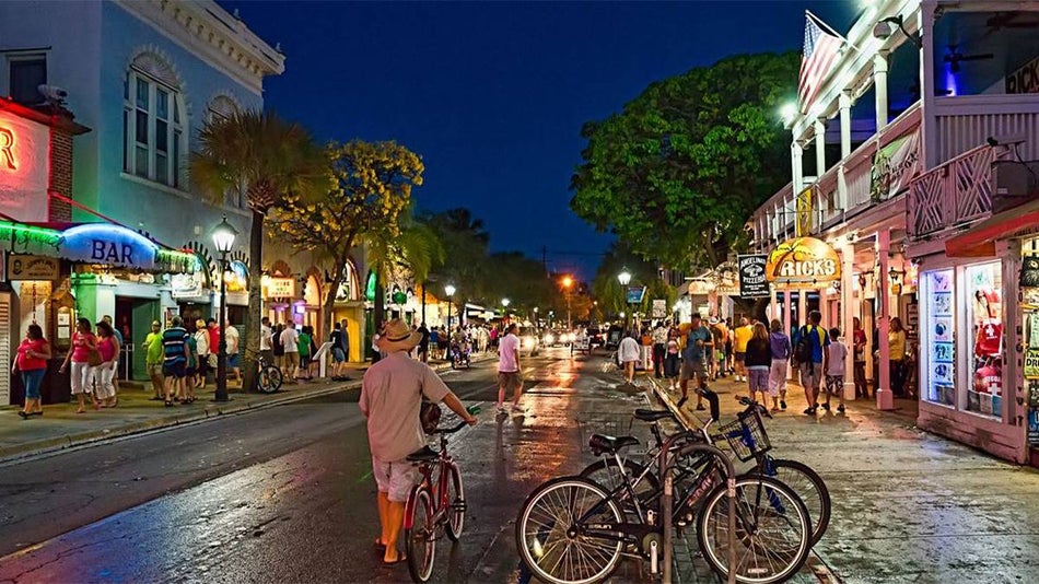 Wide shot of Duval St at night filled with people, bikes, and bright lights in Key West, Florida, USA