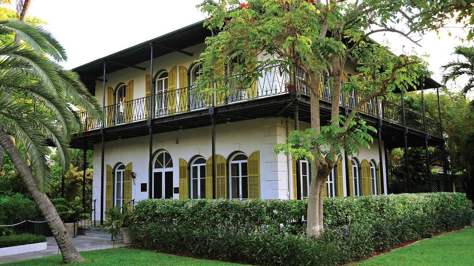 View of two sides of the Hemingway House, a white stone house with black roofs and walkways and yellow shutters in Key West, Florida, USA