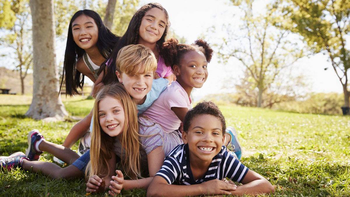 Multi-ethnic group of kids lying on each other in a park