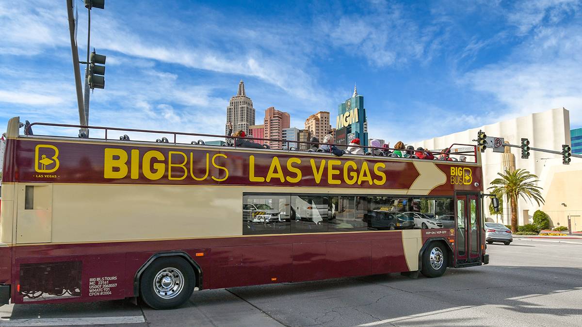 Tour bus full of people going through a intersection with a bright blue and cloudy sky above them in Las Vegas, Nevada