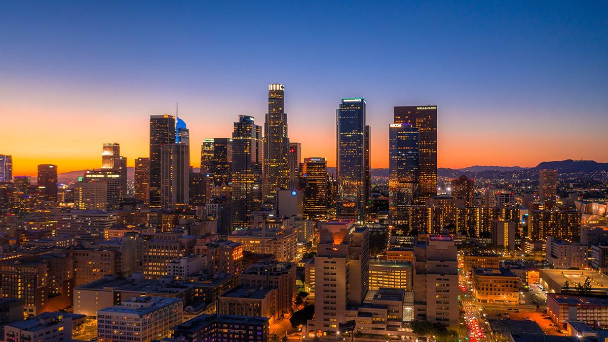 Skyline of downtown LA with a dark purple to bright orange sunset in the distance in Los Angeles, California