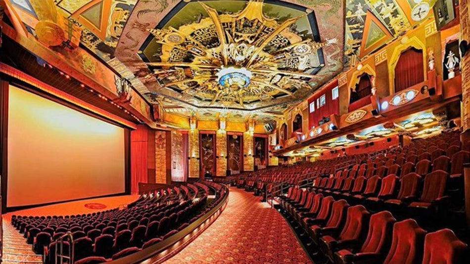The inside of the Chinese Theatre with a ornate ceiling of different shades of yellow and red velvet seats blanket the floor area in Los Angeles, California