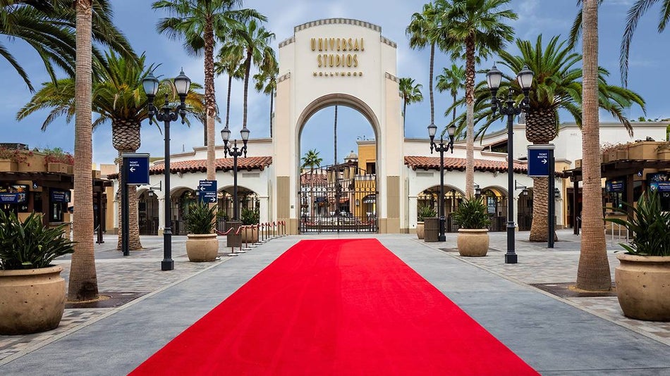 A bright red carpet rolled out in front of the gate to get into Universal Studios Hollywood with tall palm trees lining the sides of the carpet in Los Angeles, California