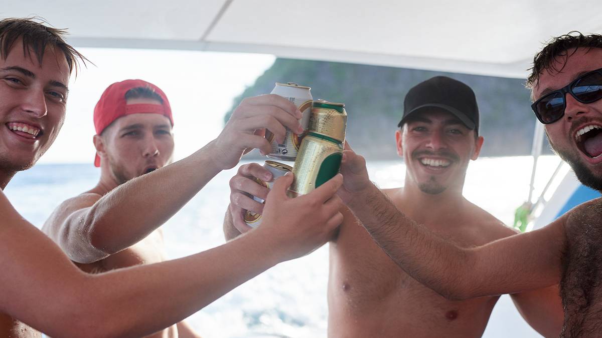 Close up of four young men cheering their beers on a boat on a a sunny day