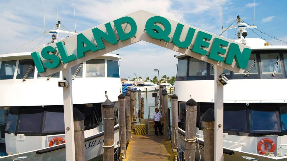 Two white boats on either side of a wood docks with a boat employee in between them and a sign close up in the photo that says "Island Queen" in Miami, Florida