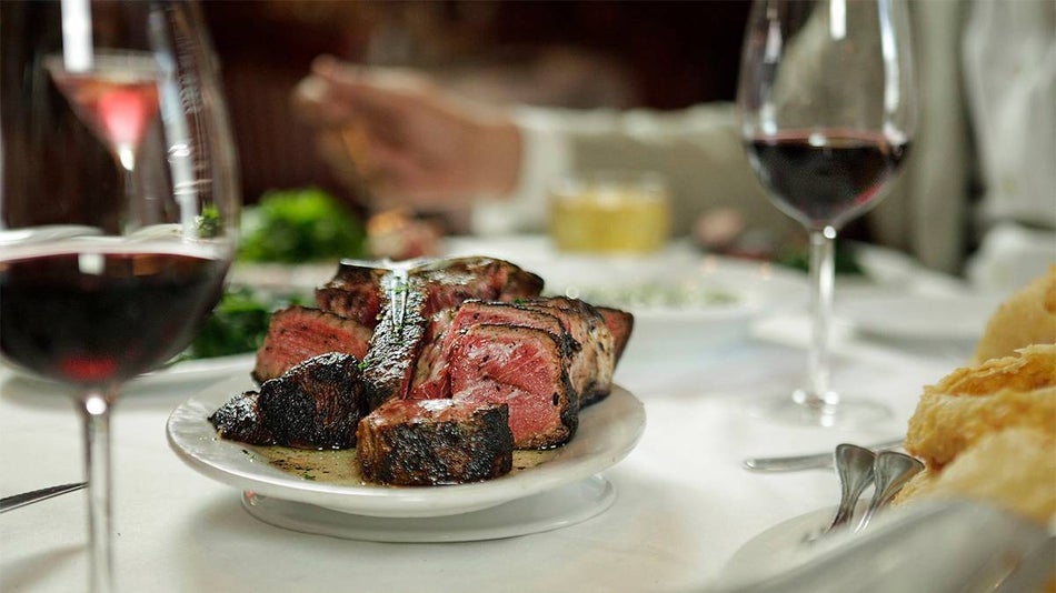 Close up photo of a cut steak and two glasses of wine with someone eating in the background at New York Prime in Myrtle Beach, South Carolina, USA